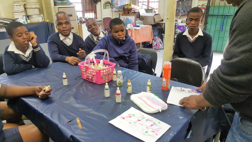 21. Mason Lincoln art room shaving foam and ink art class: Njabulo demonstrating how to make prints from paint dropped on shaving fom in tray.