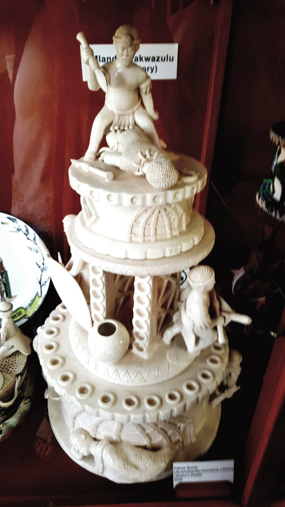 48. Ardmore Ceramics King Shaka: White intricate ceramic statue, King Shaka stands with his raised spear on the top tier. The bottom tier has traditional symbols of the Zulu nation such as the beer pot.