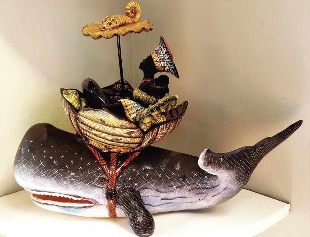 50. Ardmore Ceramics Whale: A black woman with her traditional head dress, holding her baby and an umbrella sits in round boat strapped to the back of a whale.