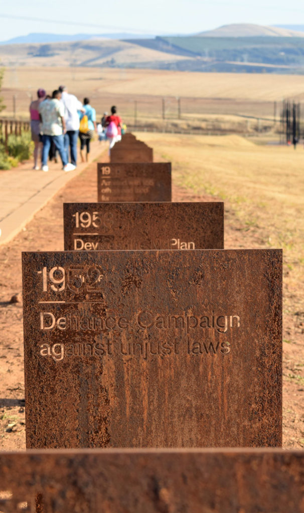 53. Howick Nelson Mandela Capture site time line: Rusting metal rectangles etched with events from Mandela’s life follow the path tourists walk towards the sculpture with the hills in the background.