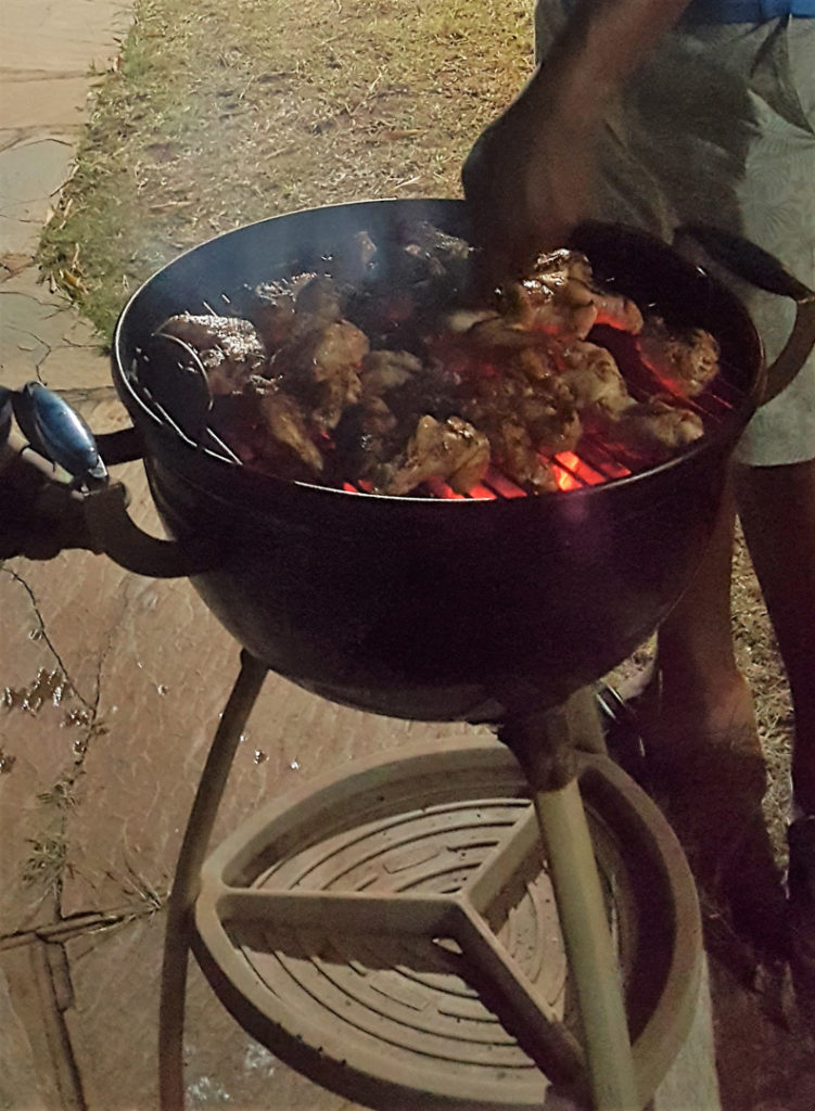 78. Food Braii Mzukulu cooking: Close up of kettle barbeque and Mzukulu’s hand as he turns the meat.